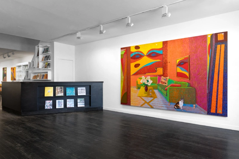 Gallery installation with a large colorful interior painting and a counter displaying smaller works.