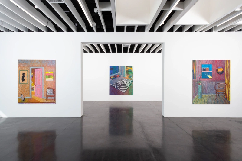 Three colorful interior paintings displayed across adjoining white gallery rooms.