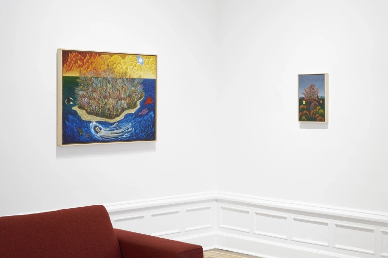 Two landscape paintings displayed above red seating in a white gallery.
