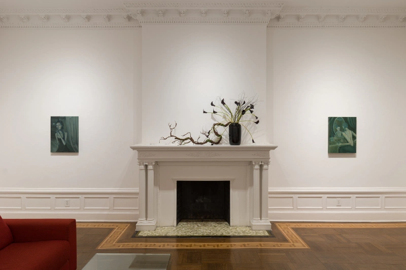 Two dark figurative paintings flanking a fireplace with a sculpture on the mantel.